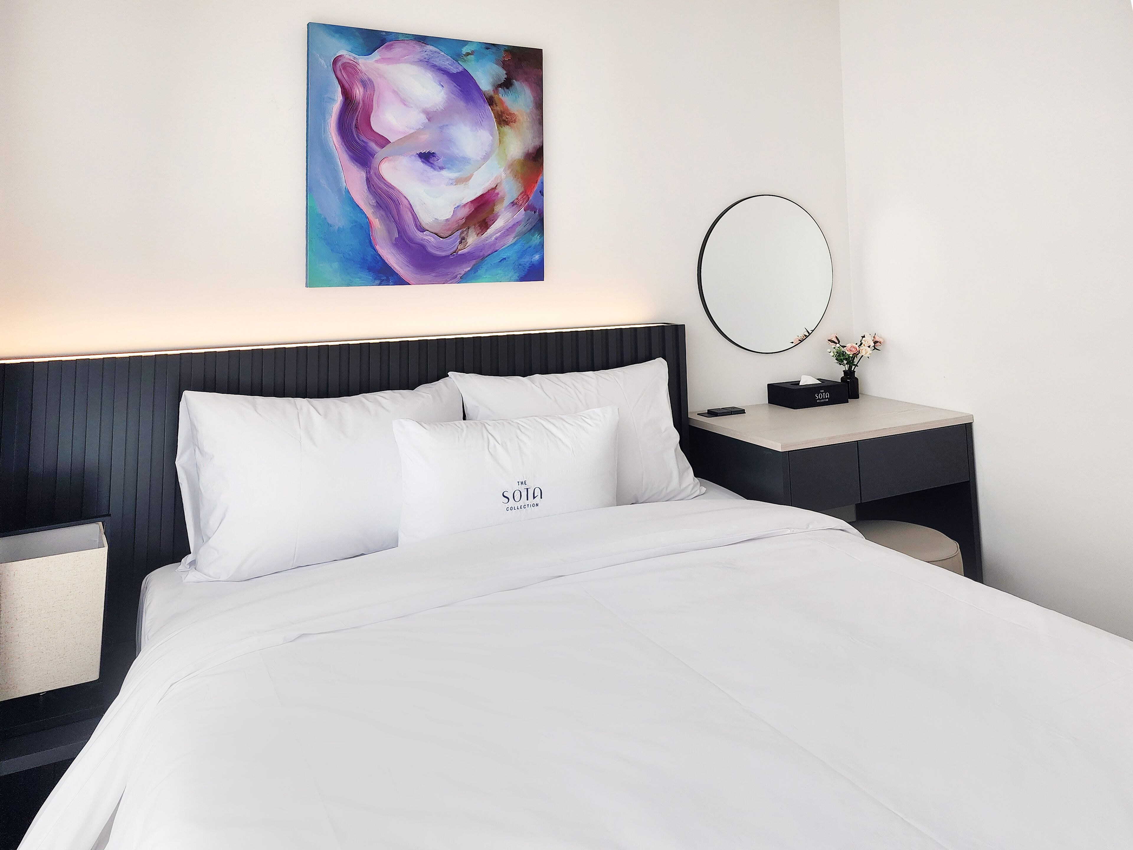Ein Hotelzimmer mit einem Bett, einem Nachttisch mit Spiegel, einem kleinen Tisch mit einer Vase und einem Bild an der Wand.