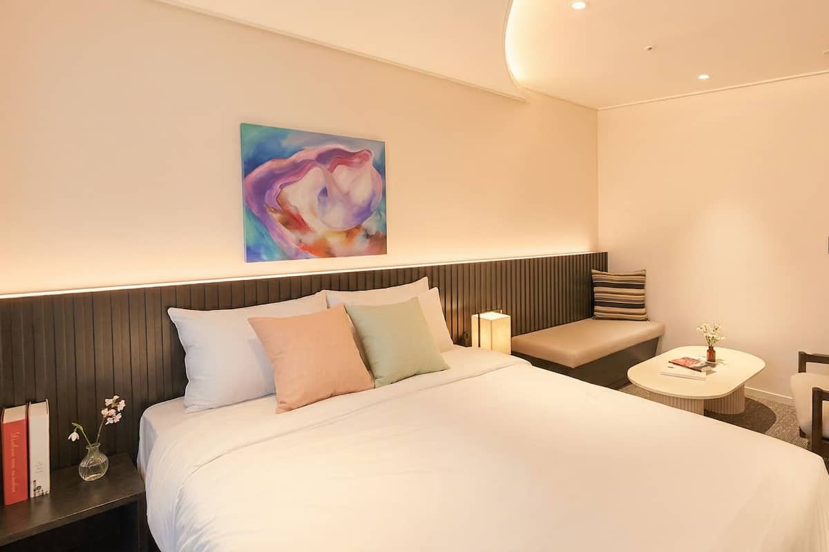 Une chambre d’hôtel avec un lit, une table de chevet, une chaise et un tableau au mur.