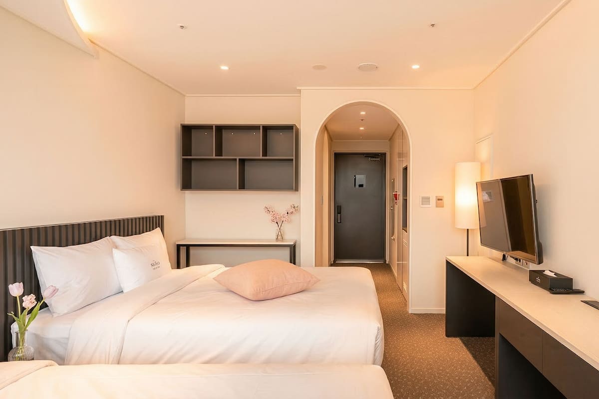 Une chambre d’hôtel comprenant un lit, des tables de chevet, une télévision, un miroir et une porte donnant sur un couloir.