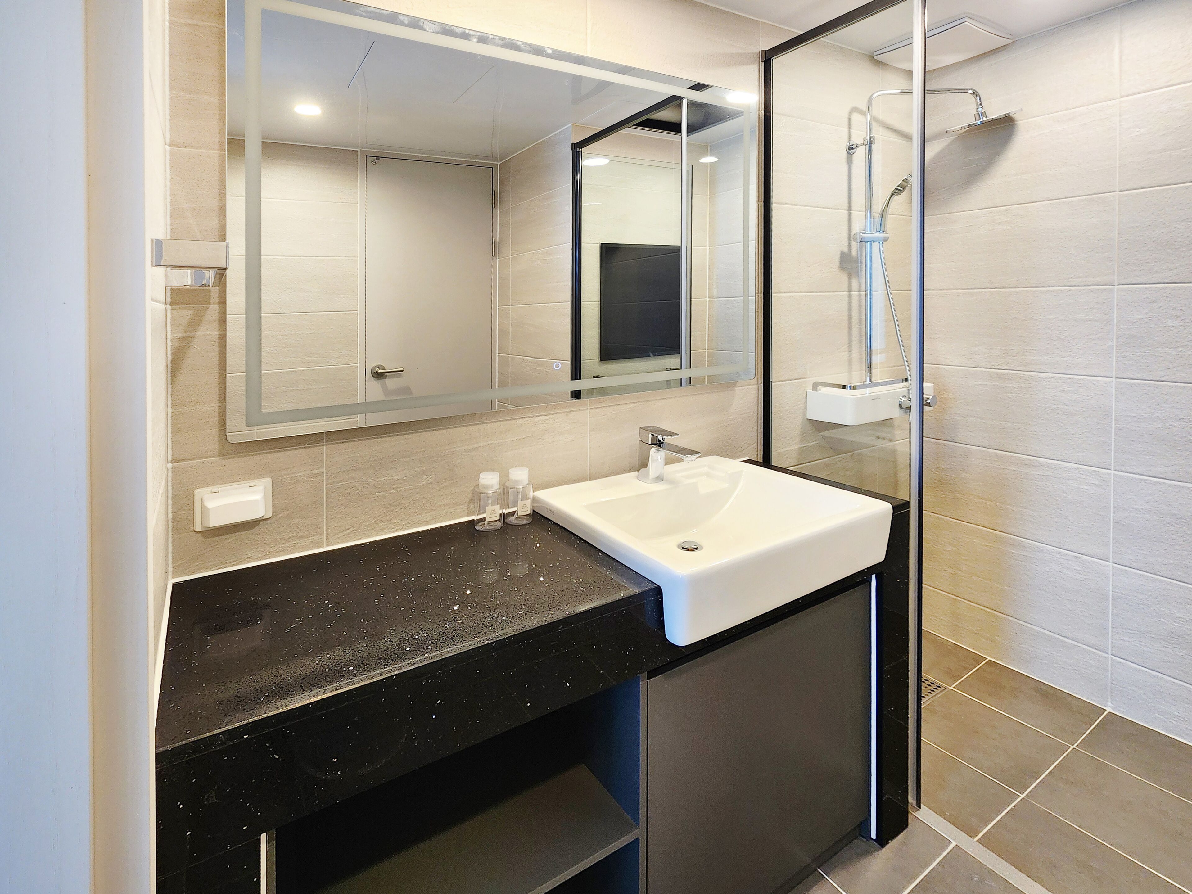 A modern bathroom with a black countertop, white sink, and a glass-enclosed shower.