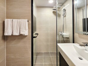 Une salle de bain moderne avec une douche en verre, un lavabo blanc et deux serviettes suspendues sur un porte-serviettes.