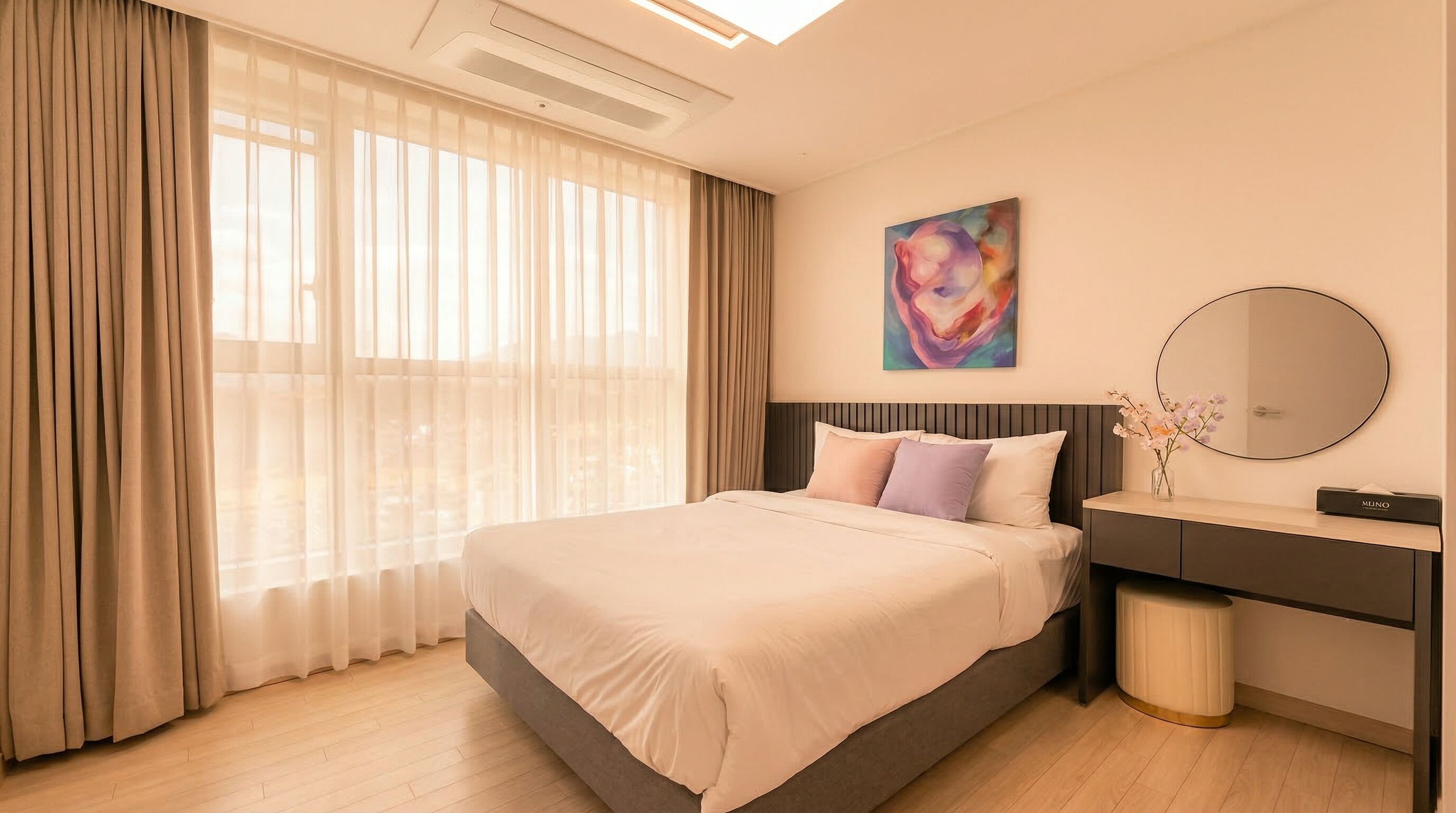 A hotel room with a bed, a bedside table, a mirror, a painting, and a window with curtains.