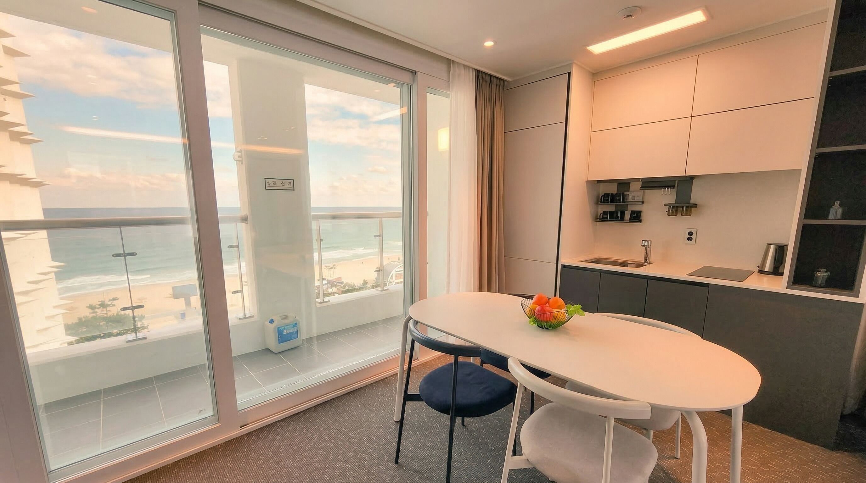 Een moderne kamer met balkon, een tafeltje met stoelen en een kitchenette.