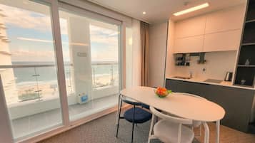 Een moderne kamer met balkon, een tafeltje met stoelen en een kitchenette.