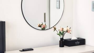Un baño con un espejo redondo, un florero negro con flores y una caja de pañuelos en la encimera con la etiqueta 'THE SOTA COLLECTION'.