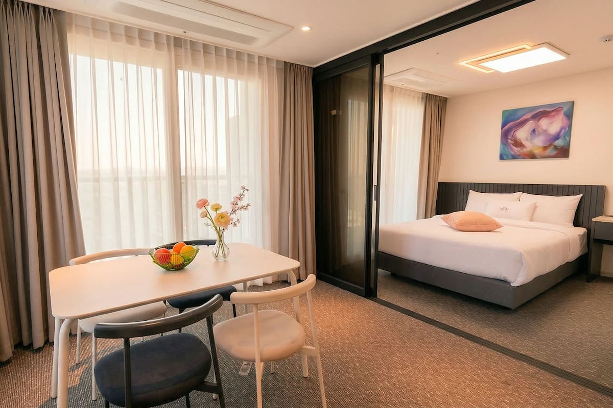 Une chambre d’hôtel avec un lit, un bureau et une chaise, un vase de fleurs et un tableau au mur.