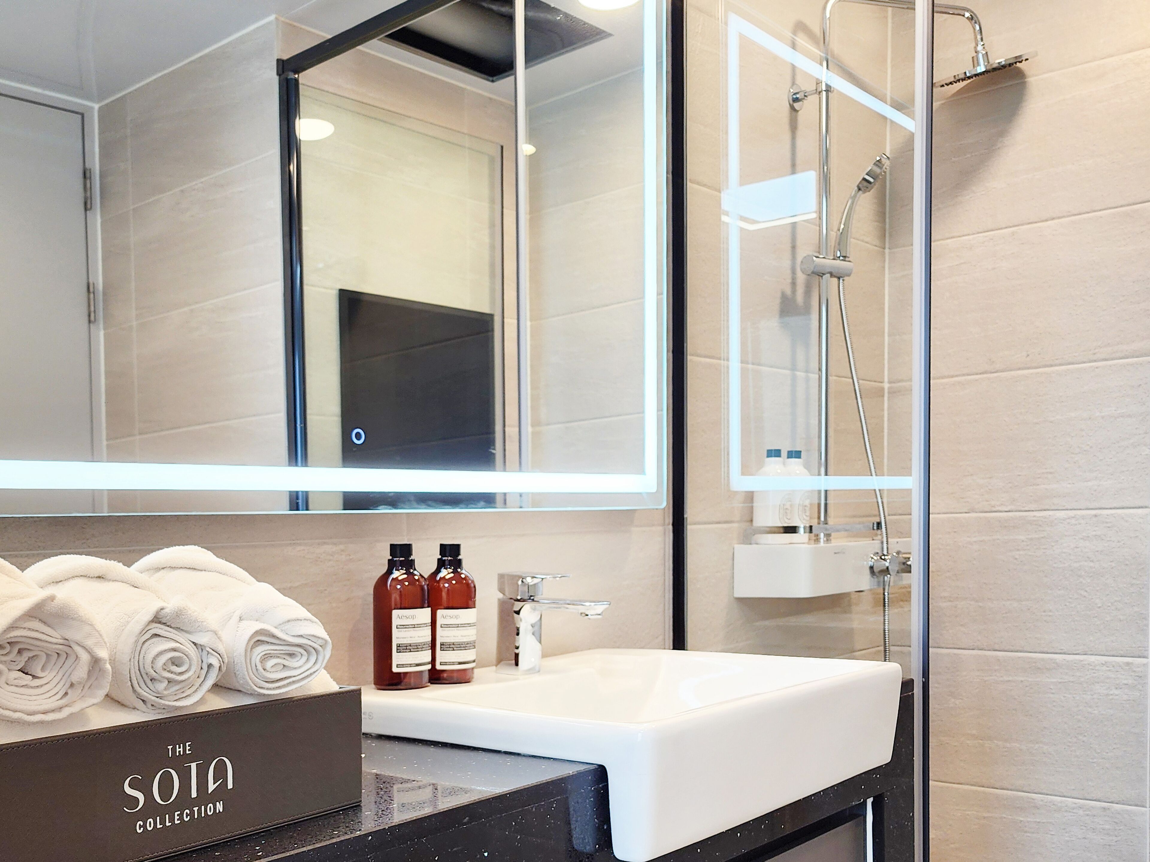 A modern bathroom with a large mirror, a white sink, and a glass-enclosed shower.