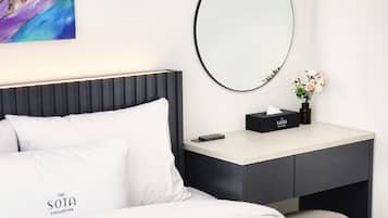 A modern hotel room with a neatly made bed, a bedside table with a tissue box and a vase of flowers, and a large mirror on the wall.