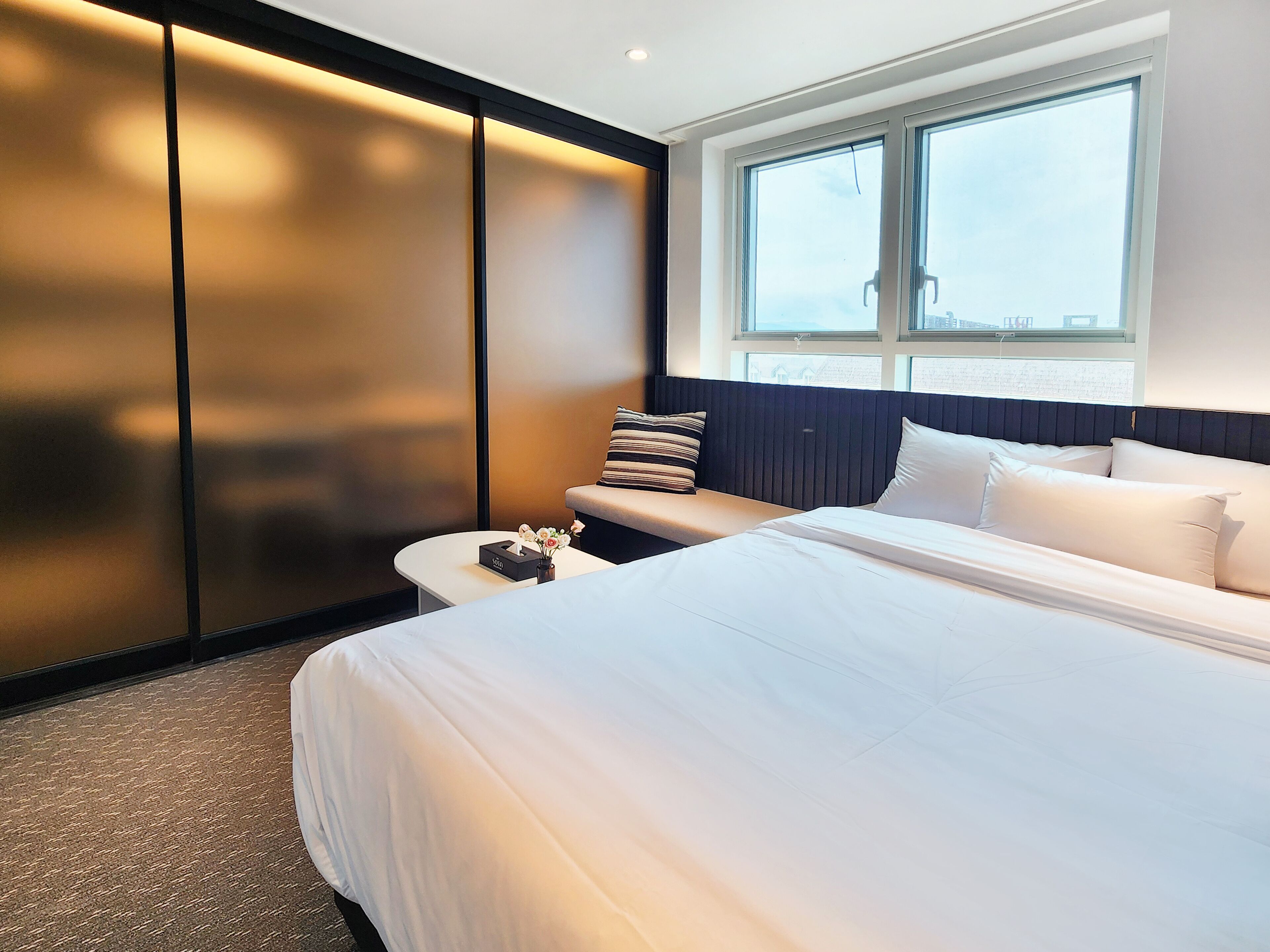 Ett modernt hotellrum med en stor säng, en sittgrupp med en bänk och ett stort fönster med utsikt.