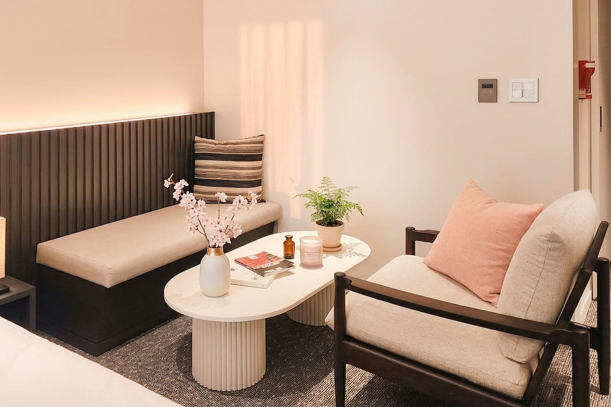 Une chambre d’hôtel avec un lit, un canapé, une petite table sur laquelle est posé un vase de fleurs, une plante en pot et une lampe de chevet.