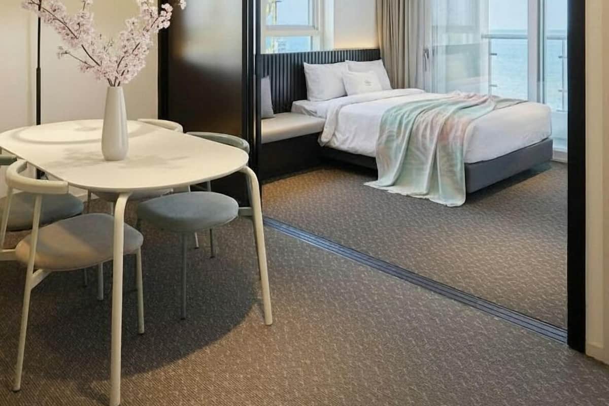 Une chambre d’hôtel avec un lit, un bureau avec des chaises, un vase de fleurs et une vue sur l’extérieur.