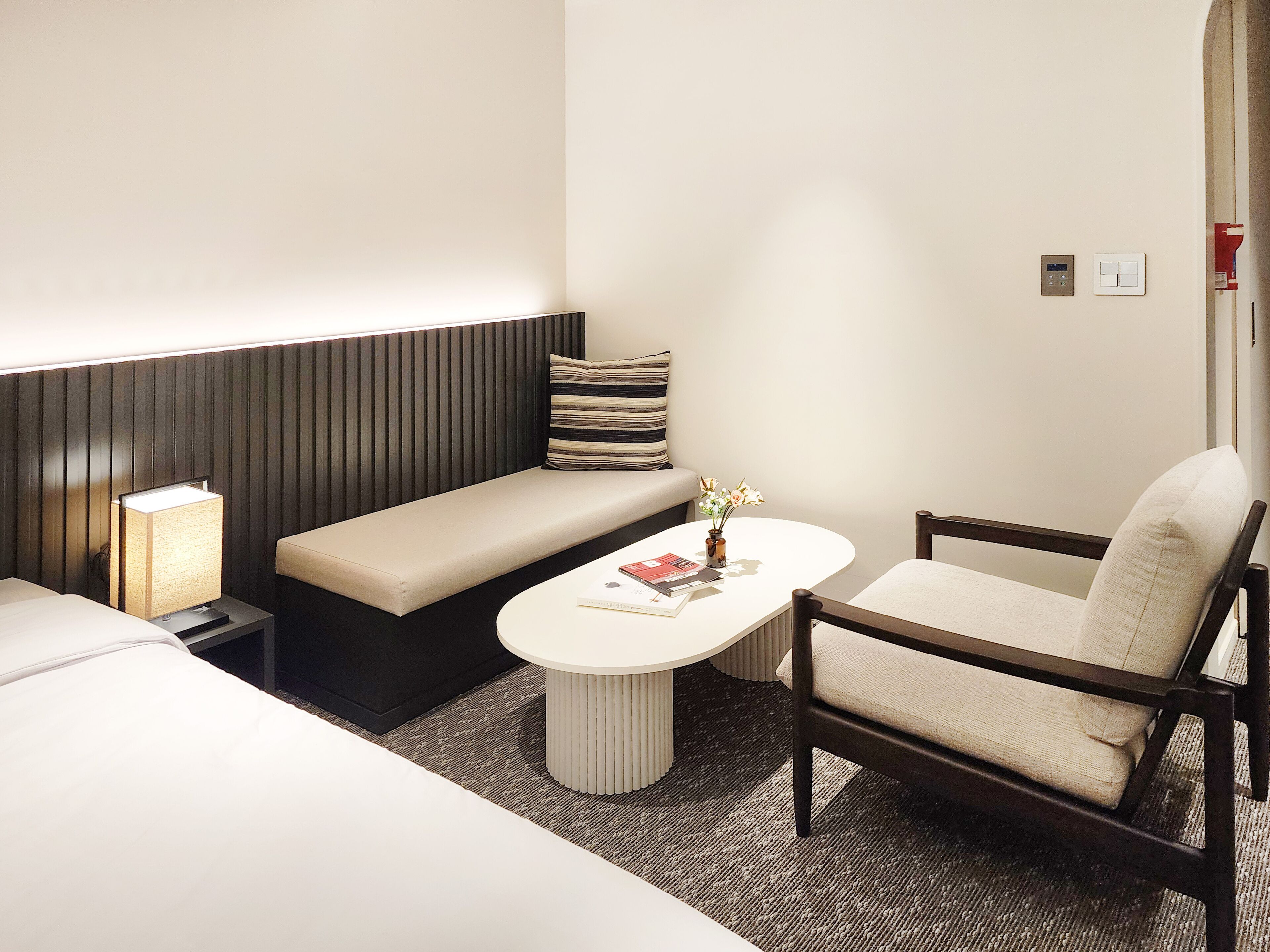 A compact hotel room with a bed, a sofa, a chair, a small table, and a bedside lamp.