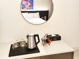 A hotel room with a bed, a bedside table with a coffee maker, wine glasses, and a box labeled "The Sota Collection".
