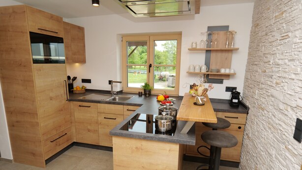 Une cuisine moderne avec des meubles en bois, un îlot central doté de tabourets, une grande fenêtre et un mur en pierre.