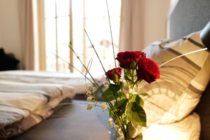 Un lit avec une literie blanche et un vase de roses rouges sur la table de chevet.