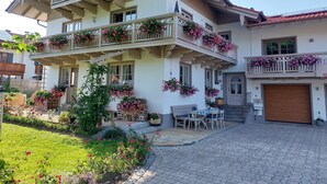 Une maison à deux étages dotée de nombreux balcons ornés de jardinières, d’une allée pavée et d’un petit espace extérieur aménagé pour s’asseoir.