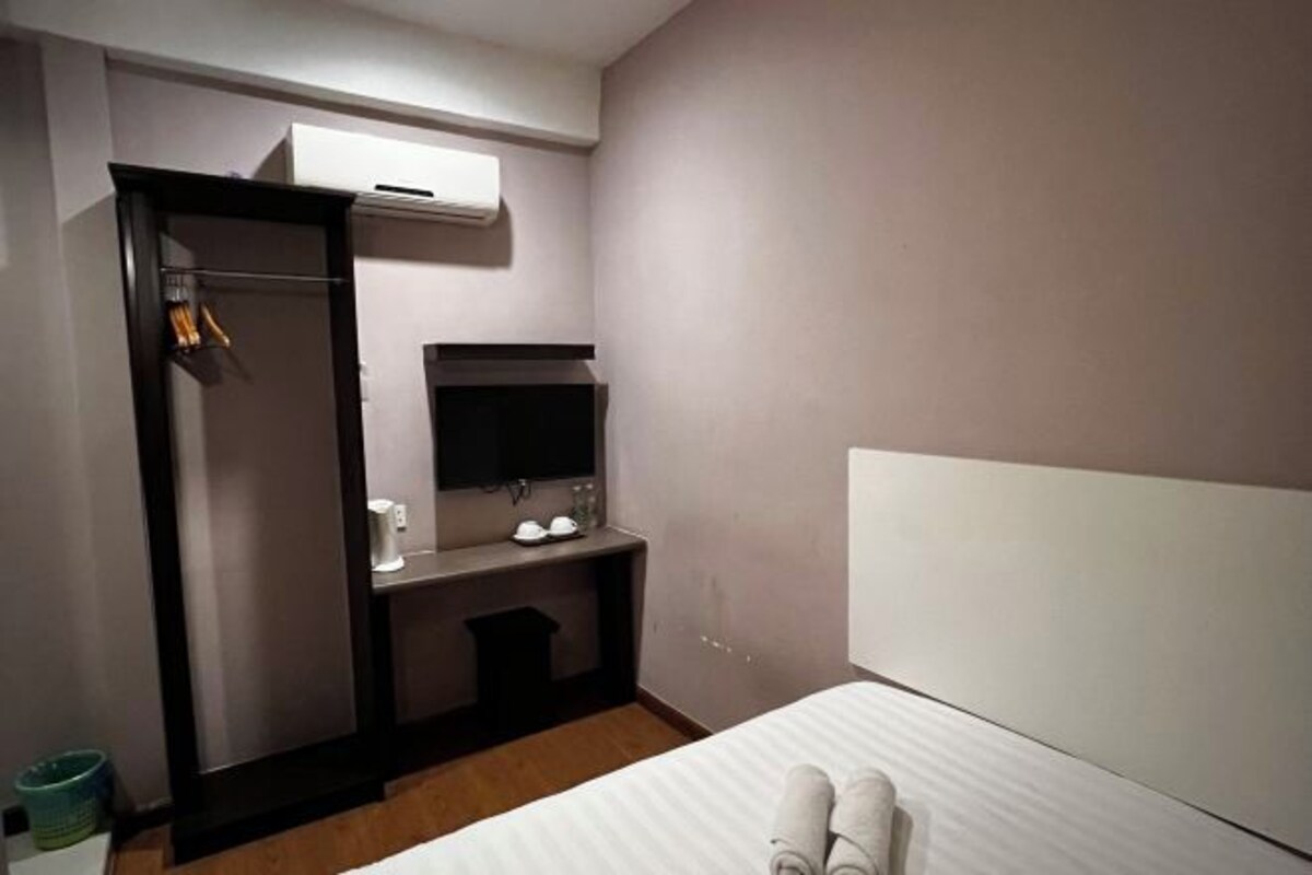 Habitación de hotel con cama, escritorio con silla, espejo, armario y aire acondicionado.