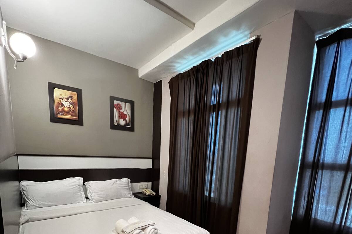 A neatly made bed with white linens and towels, a dark headboard, and two framed pictures on the wall.
