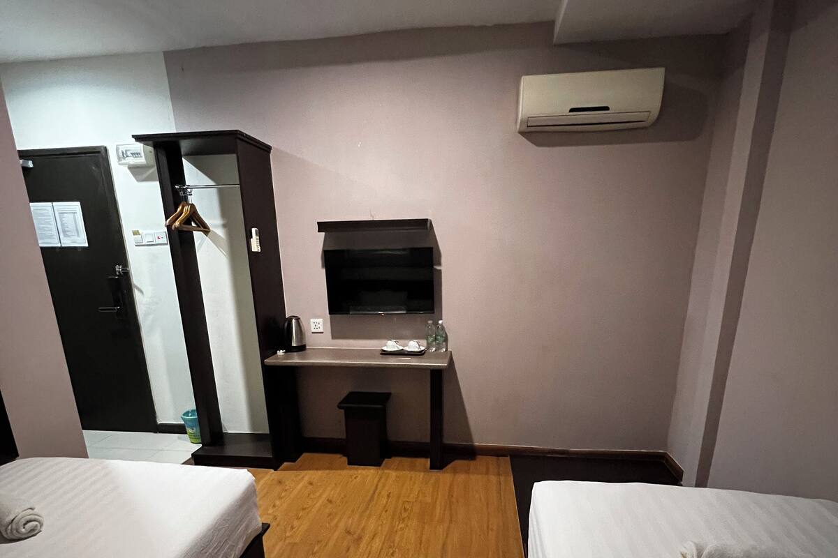 A compact hotel room with two single beds, a small kitchenette, a desk, and a wardrobe.