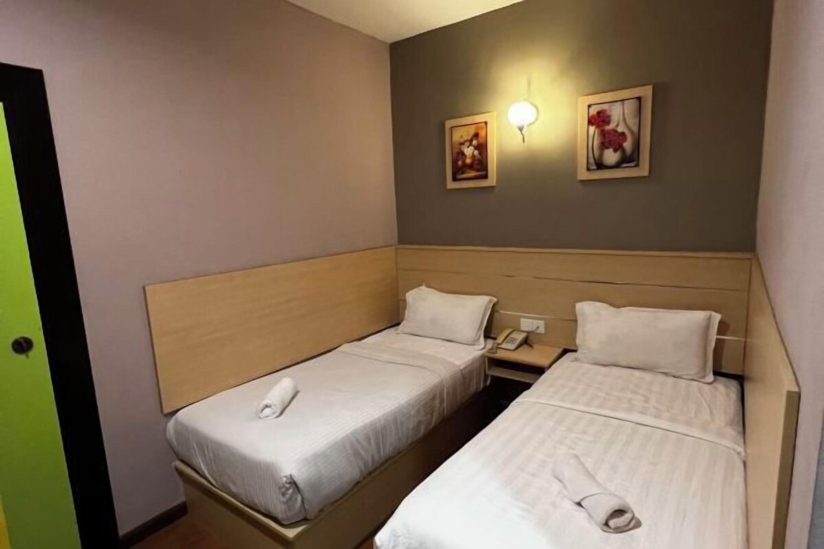 A hotel room with two single beds, a bedside table with a lamp, and a wall-mounted light fixture.