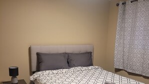 Une chambre à coucher avec un lit, une table de chevet, une lampe et une fenêtre avec des rideaux.