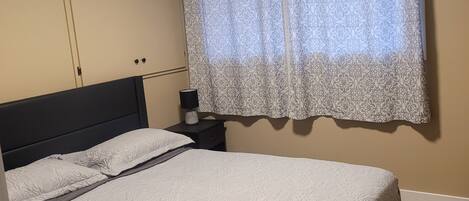 Un dormitorio con una cama, una mesita de noche, una lámpara y una ventana con cortinas estampadas.