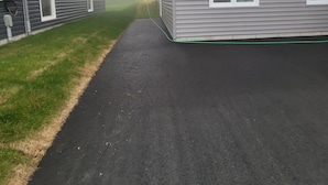 Une allée menant à une maison à deux étages, avec un garage dont la porte est visible et une petite fenêtre.