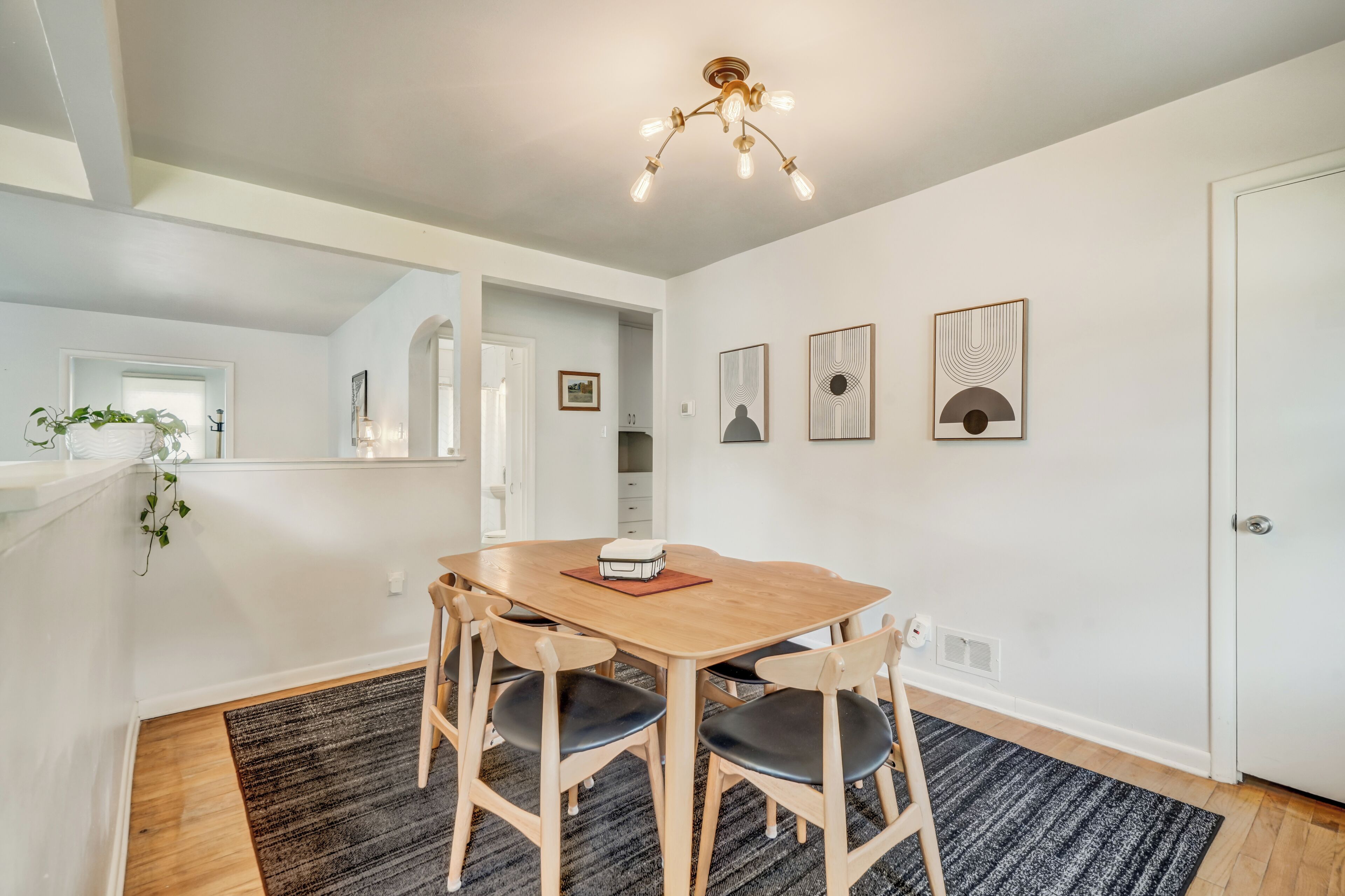A dining area with a wooden table and chairs, a chandelier, and framed artwork on the wall.