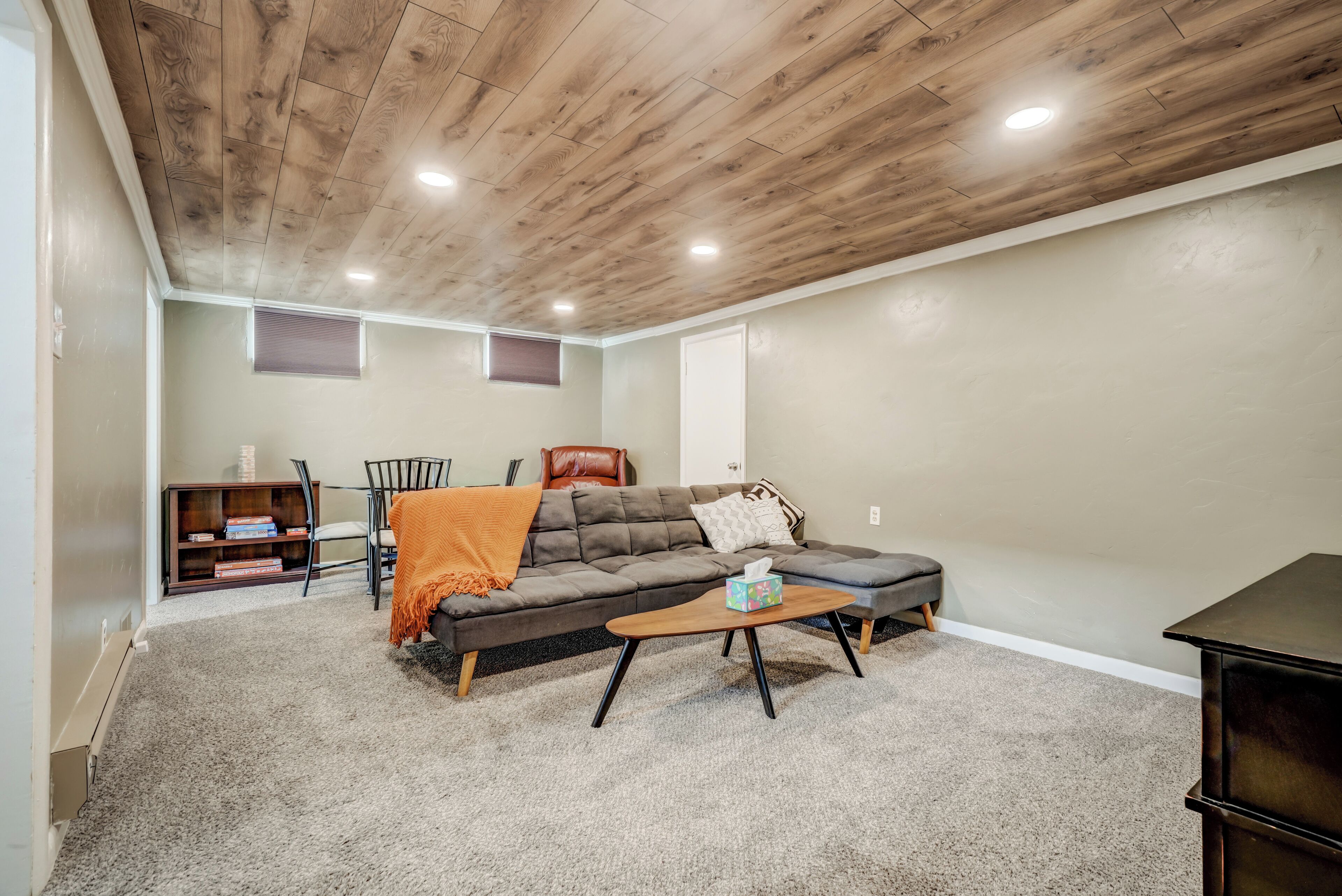 A cozy living room with a wooden ceiling, a grey sofa, a coffee table, and a bookshelf.