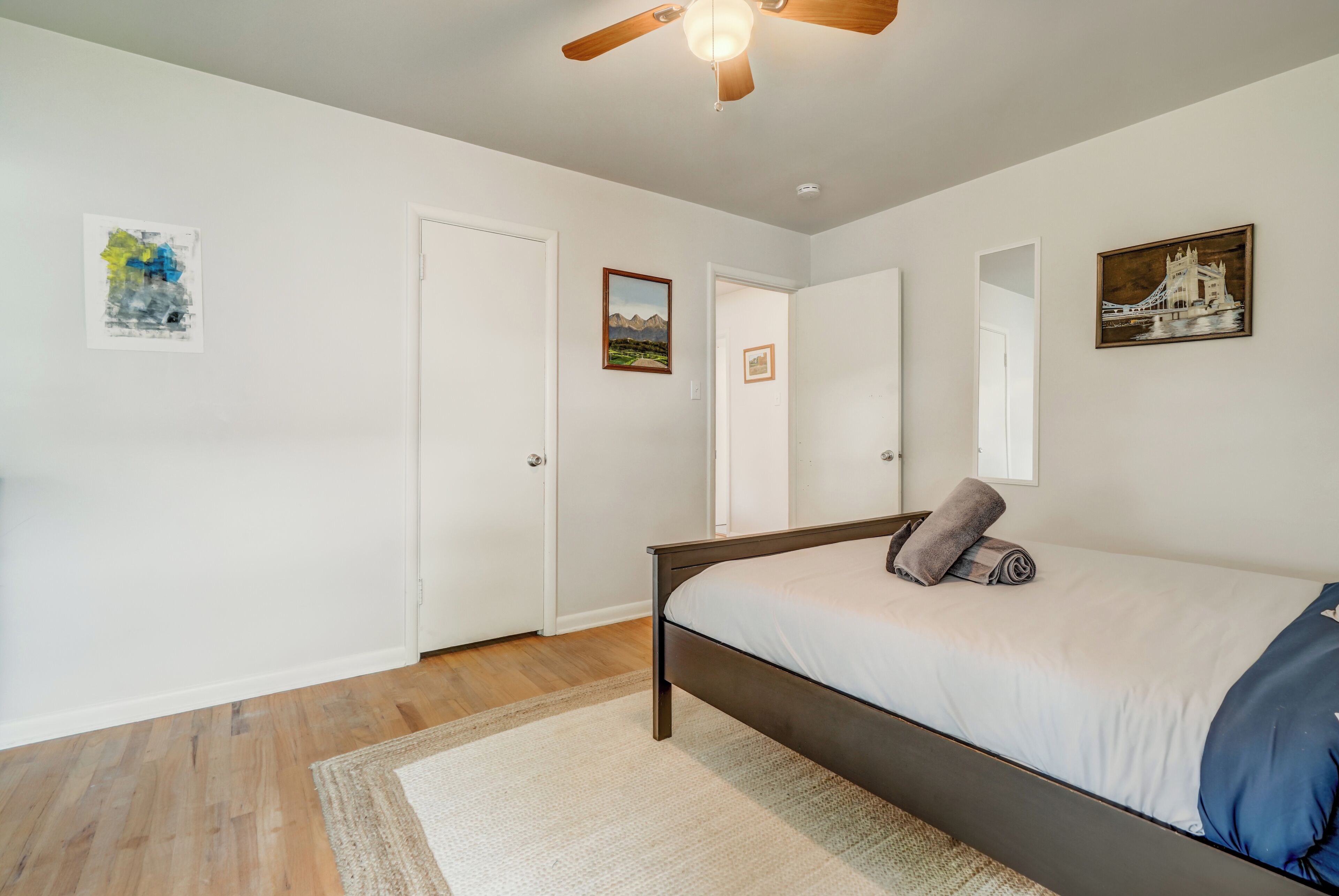 A bedroom with a bed, a ceiling fan, a rug, and framed pictures on the walls.
