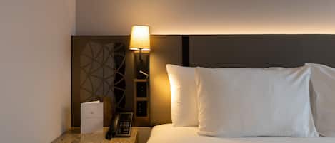 A hotel room with a bed, a nightstand with a lamp, a telephone, and a card on the nightstand.