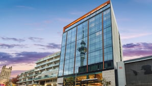 A modern hotel with a glass facade, a prominent tower, and a historic building in the background.