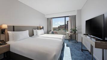 A hotel room with a large bed, a TV, a desk, and a view of the city.