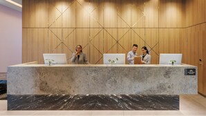 A reception desk with three staff members, a wooden wall with a geometric pattern, and a sign indicating a bicycle storage area.
