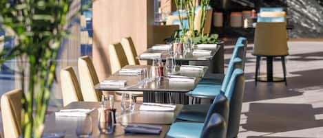 A restaurant with long tables, chairs, and potted plants.