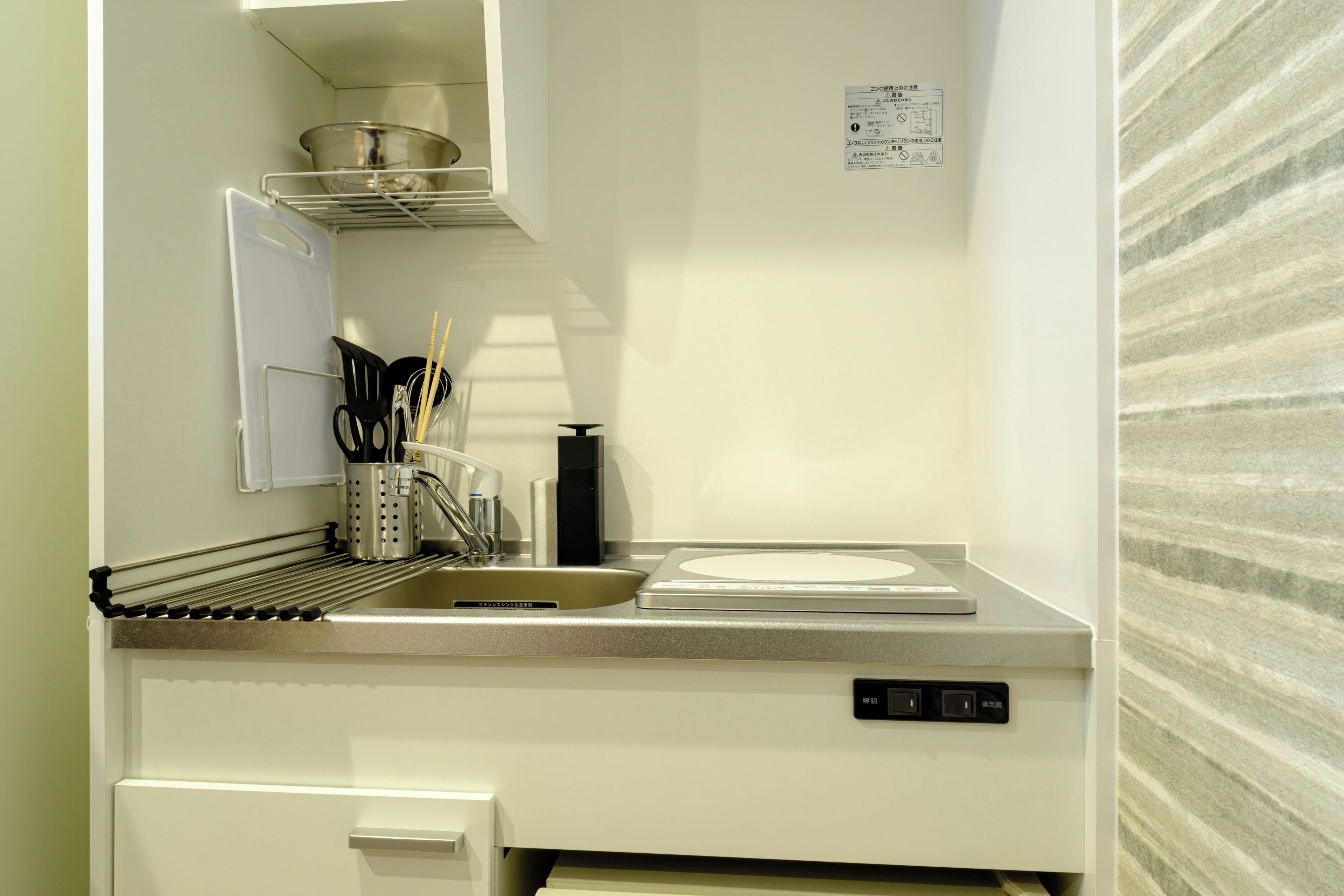 A compact kitchen with a sink, stove, and utensil holder.