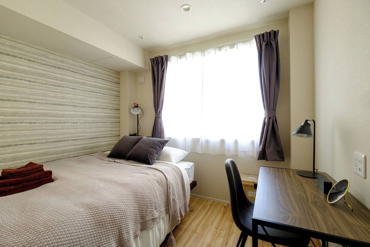 A bedroom with a bed, a desk, a chair, a lamp, and a window with curtains.