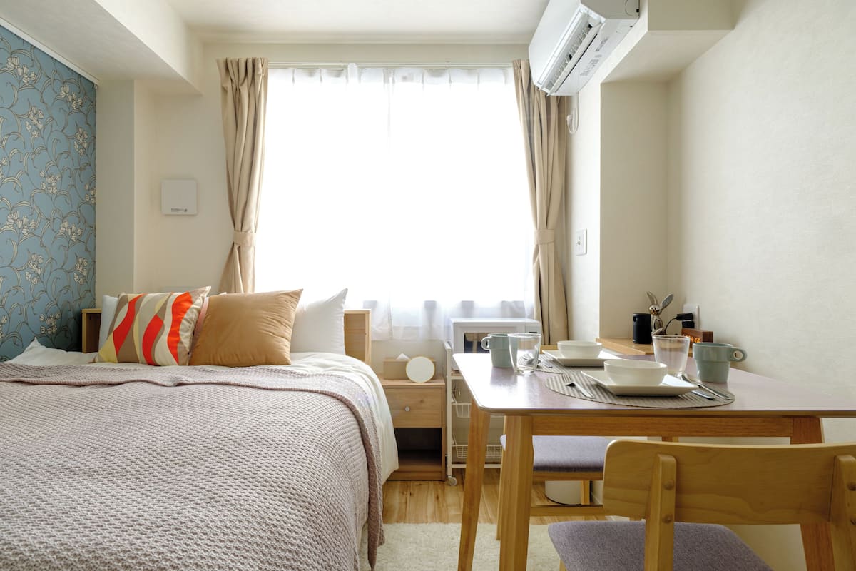 A hotel room with a bed, a table with a cup and a plate, and a window with curtains.