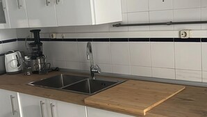 A modern kitchen with white cabinets, a wooden countertop, a double sink, and a coffee maker.