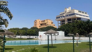 A swimming pool with a green fence, surrounded by grass and trees. There are buildings in the background.