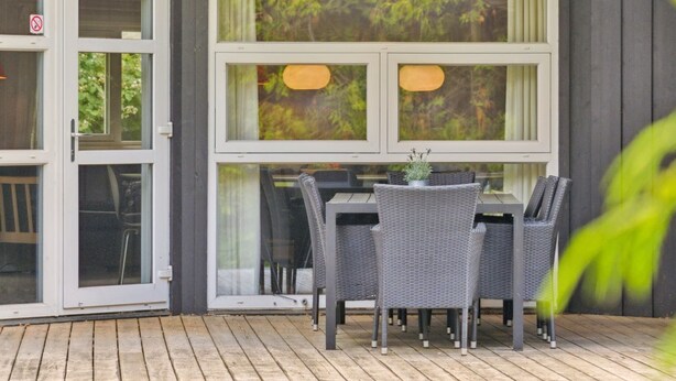 An outdoor dining area with a table and chairs, large windows, and a wooden deck.