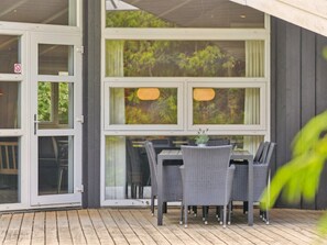 Un espace extérieur aménagé pour les repas, avec une table et des chaises, de grandes fenêtres et une terrasse en bois.
