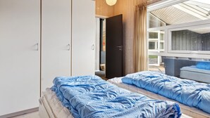 A bedroom with two beds, wooden walls, a wardrobe, and a large window.