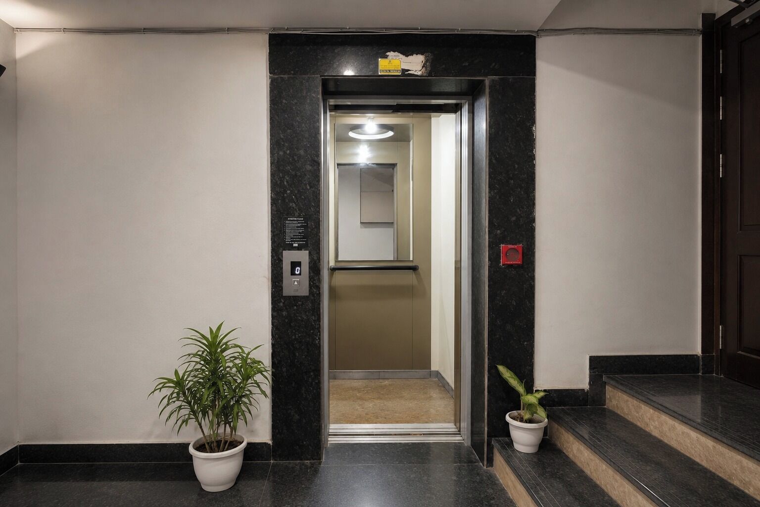 An elevator entrance with a digital display, a potted plant, and a marble floor.