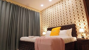 Un dormitorio con cama, ventilador de techo, pared con diseño, mesita de noche con lámpara y alfombra morada.