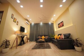 A living room with a black sofa, a coffee table, a TV, and a ceiling fan. - Lime Tree 3BHK Serviced Apartments DLF 5 (Gurugram)