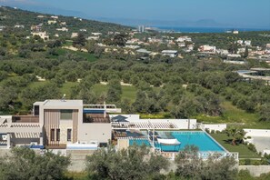 A modern building with a swimming pool, surrounded by greenery and a view of the sea.