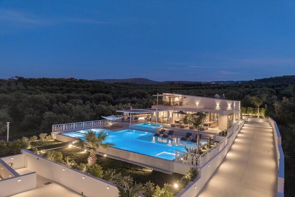 Eine moderne Villa mit Swimmingpool, Sitzgelegenheiten im Freien und Blick auf die umliegende Landschaft.