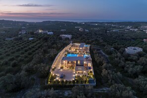 An aerial view of a modern residential property with a swimming pool, multiple buildings, and surrounding greenery.