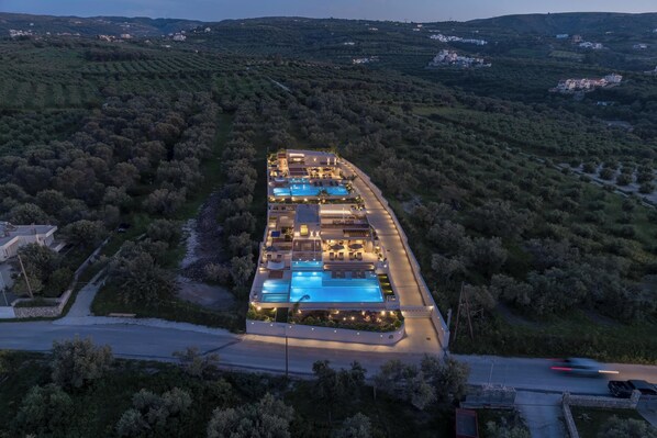 A modern resort with a swimming pool, multiple guest rooms, and a view of the surrounding hilly landscape.